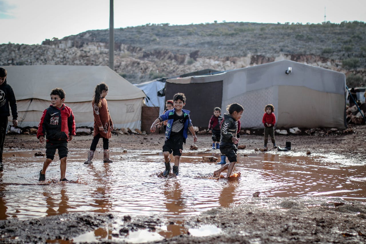 services-03 Kids enjoying playtime in a muddy refugee camp in Idlib, Syria amidst challenging conditions.