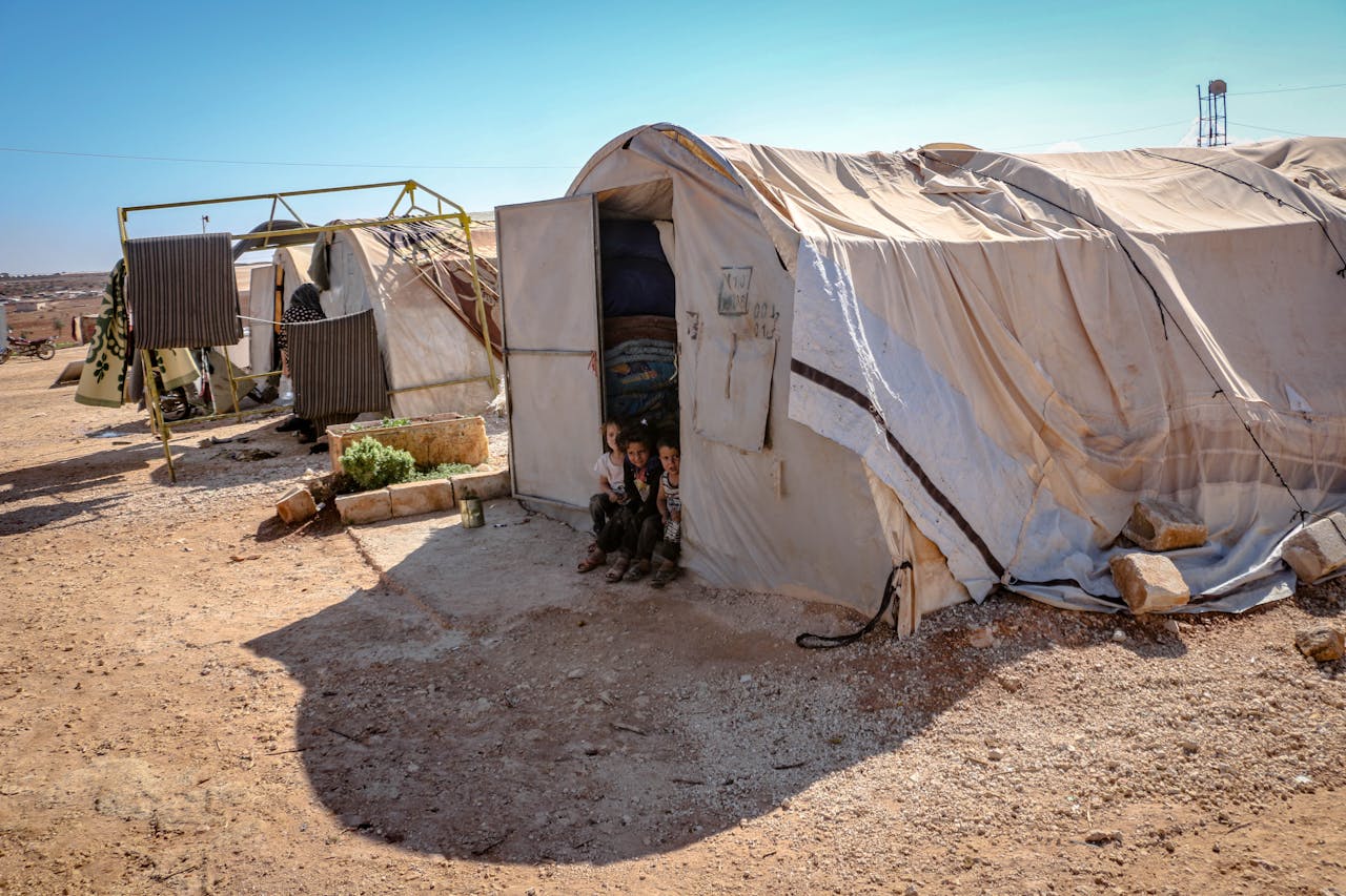 about-us Young children standing near tents in a refugee camp in Idlib, Syria. Focus on poverty and displacement.